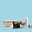 Hair styling tools including a brush, bottle, and box on a light blue background